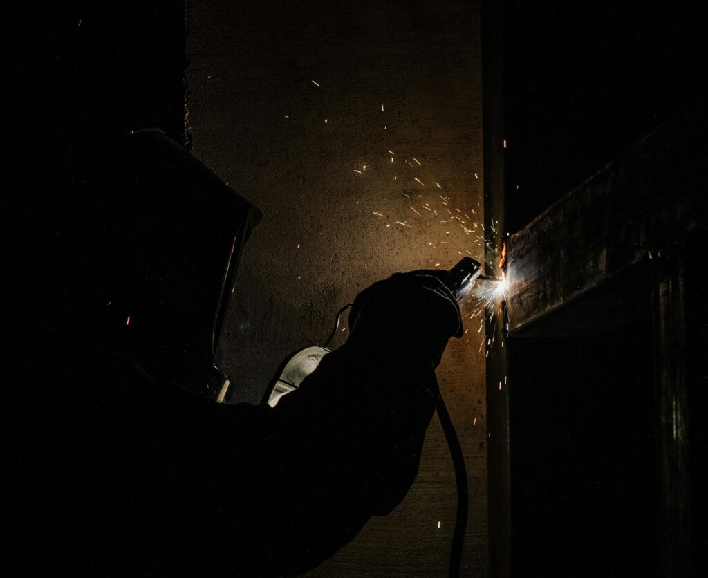 Silhouette of a welder creating bright sparks in a dark workshop environment.
